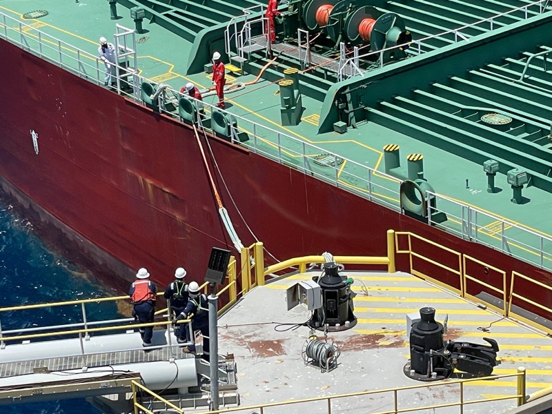 A mooring team in hard hats and coveralls on a berthing dolphin as a tanker comes alongside, Grand Bahama.