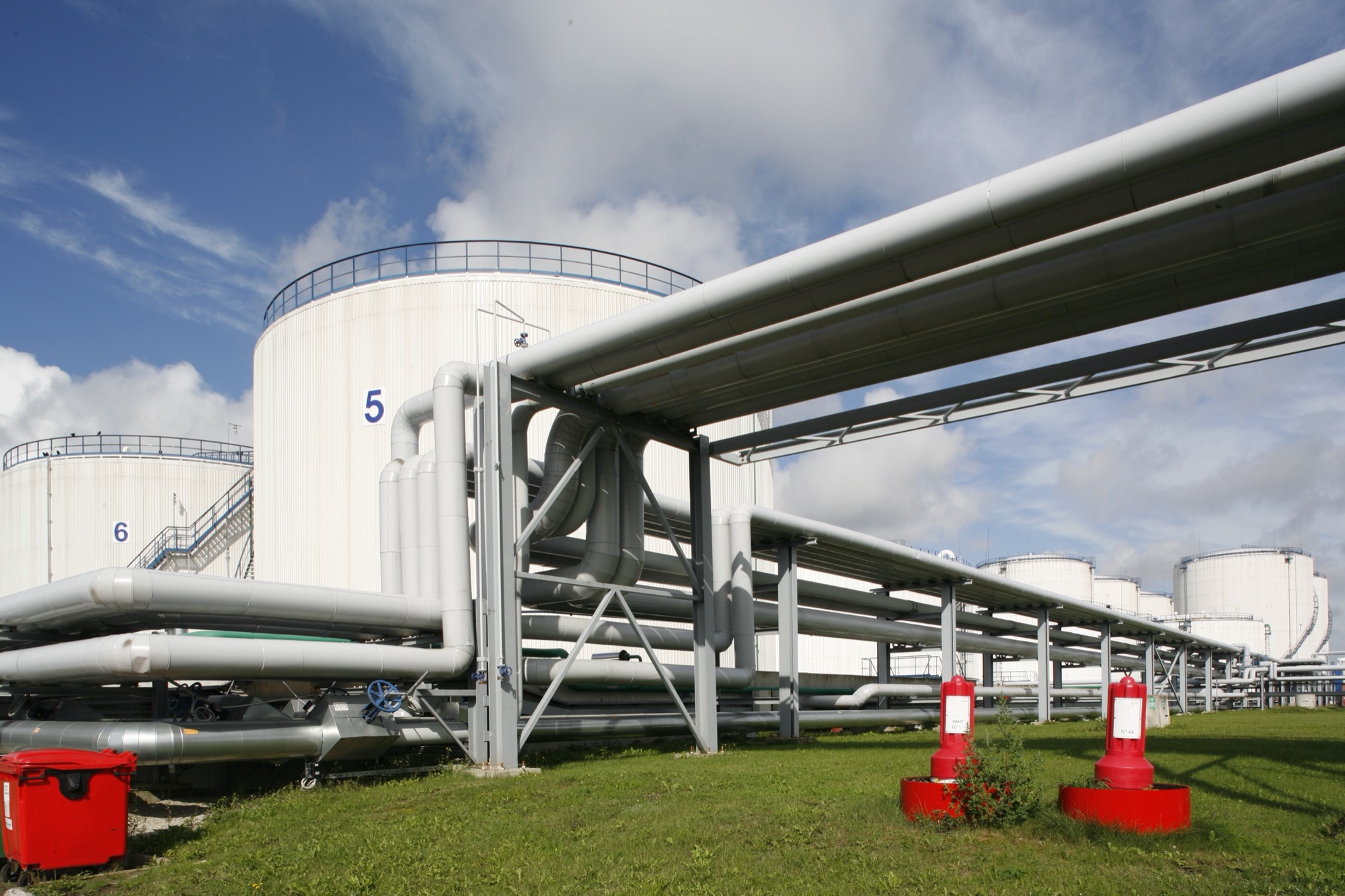 Storage tanks and an elevated pipe rack at Liwathon E.O.S. in Muuga, with fire monitors on the grass.